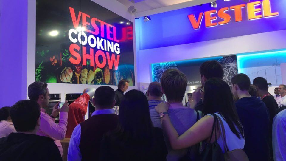 Visitantes reunidos em torno de um show de culinária.